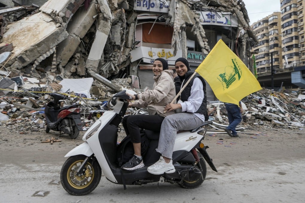 Women on a scooter hold a Hezbollah flag as they drive past a destroyed building in Beirut on Wednesday following the ceasefire between Israel and Hezbollah. Photo: AP