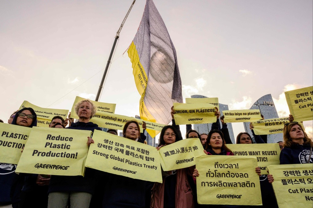 A flag with an eye and writing that reads: ‘Governments, the world is watching, cut plastic production now’ above Greenpeace activists holding placards in Busan on Monday. Photo: AFP