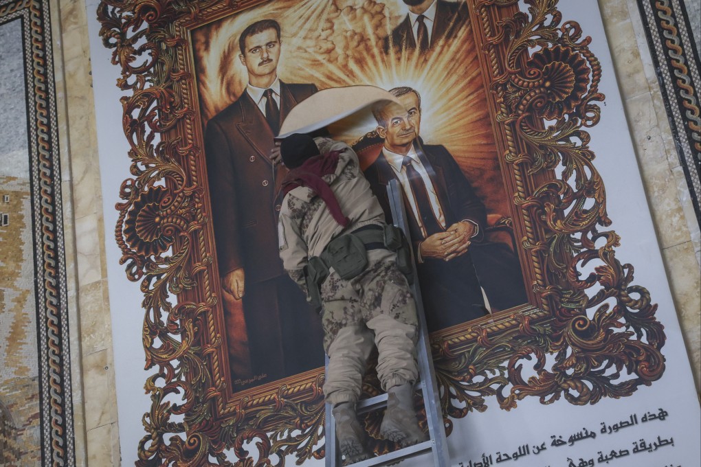 A Syrian opposition fighter tears up a painting depicting Syrian President Bashar al-Assad and his late father Hazef Assad at the Aleppo international airport. Photo: AP