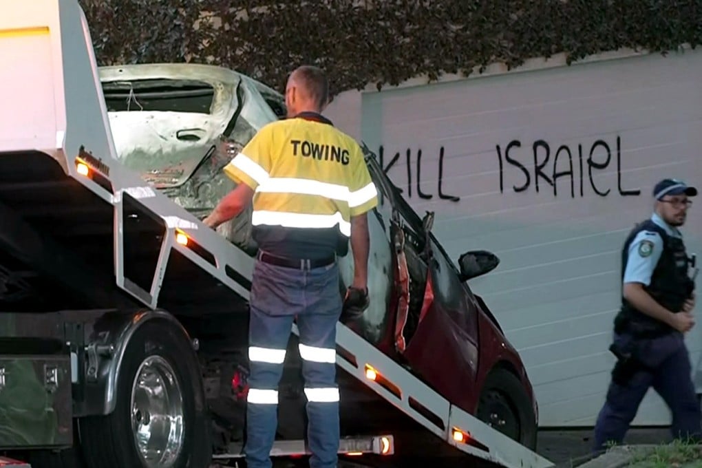 A torched car is removed in the Sydney suburb of Woollahra on Wednesday in front of anti-Israel graffiti written on a wall. Photo: Australian Broadcasting Corporation/AFP