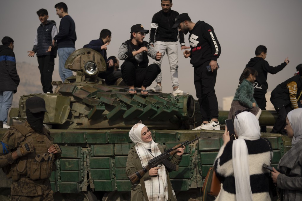 A woman holding a rifle borrowed from a Syrian opposition fighter poses for a picture, next to a government forces tank in Damascus, Syria. Photo: AP