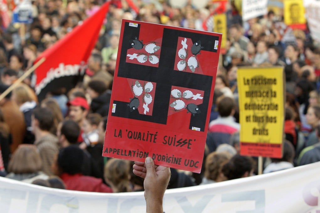 A protester at a rally against the right-wing Swiss People’s Party in September 2007 holds a card with a swastika superimposed on the party’s election poster showing a black sheep being kicked out of the country by three grinning white sheep. Photo: AFP