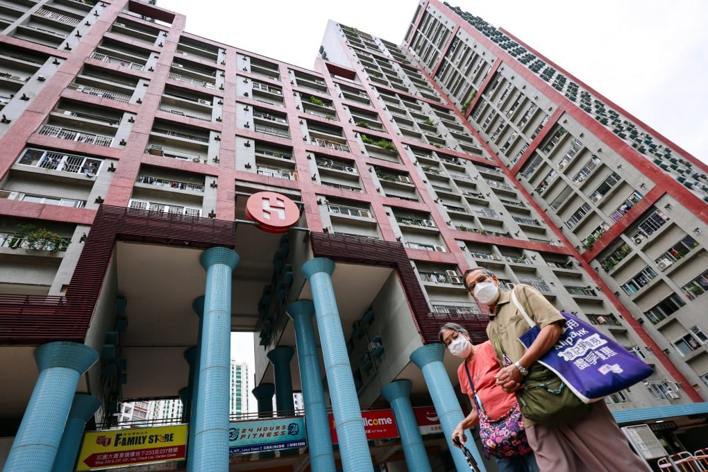 Two tenants wearing masks walk past a large public housing building with signs indicating housing policies and recovery initiatives.
