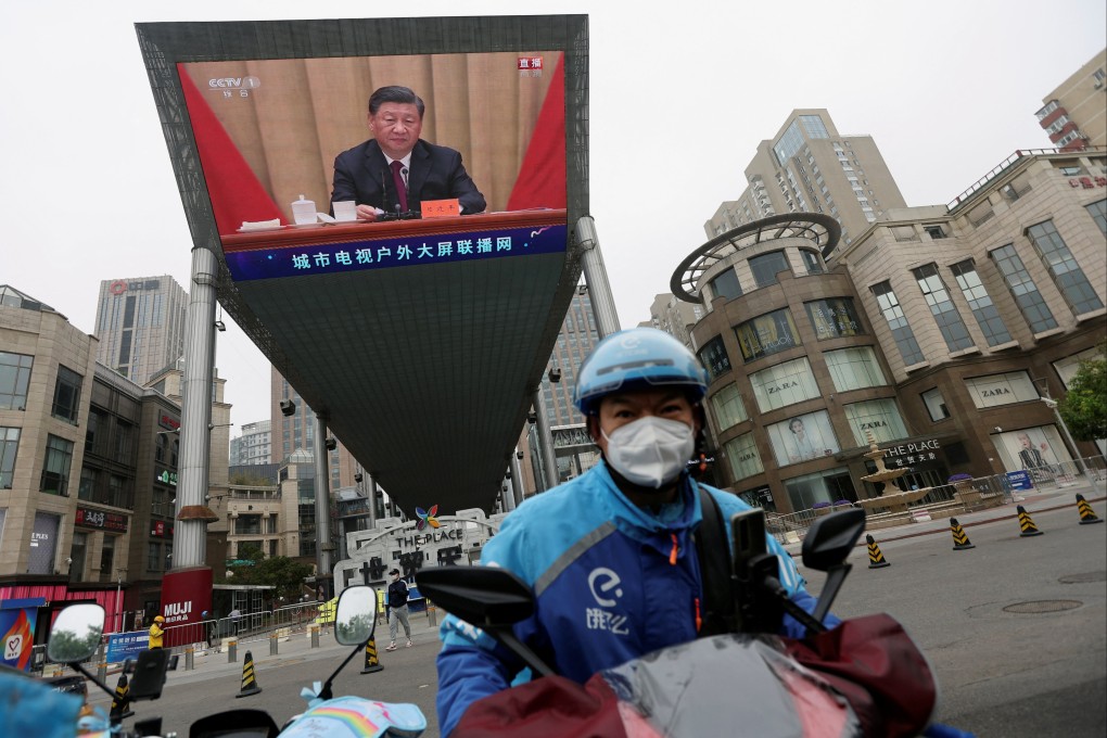 A delivery worker rides near a giant screen showing President Xi Jinping, on May 10, 2022. Photo: Reuters