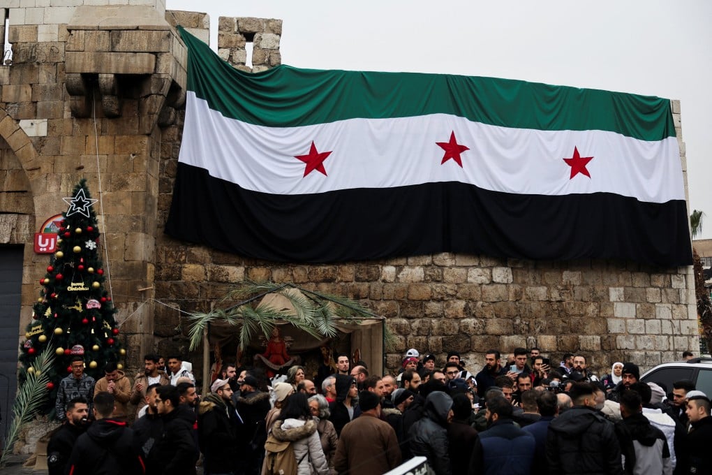 People gather near a Christmas tree and a flag adopted by the new Syrian rulers, on the day of a protest against the burning of the Christmas tree in Hama, Syria on December 24. Photo: Reuters