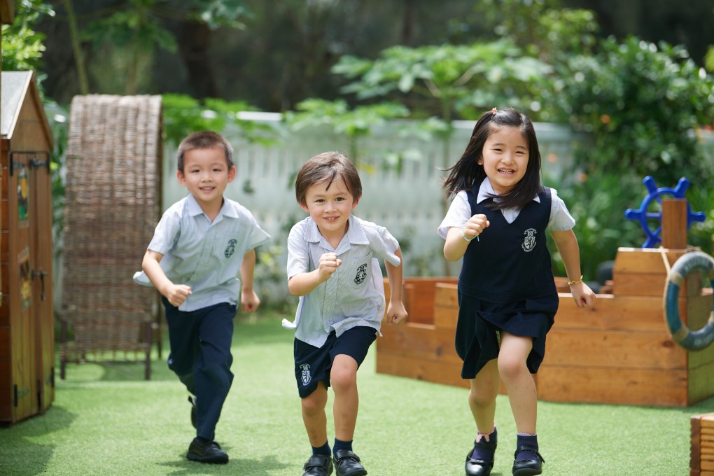 Three young children are running and smiling outdoors, with a playground and green foliage in the background, possibly indicating a school suspension or weather warning scenario.
