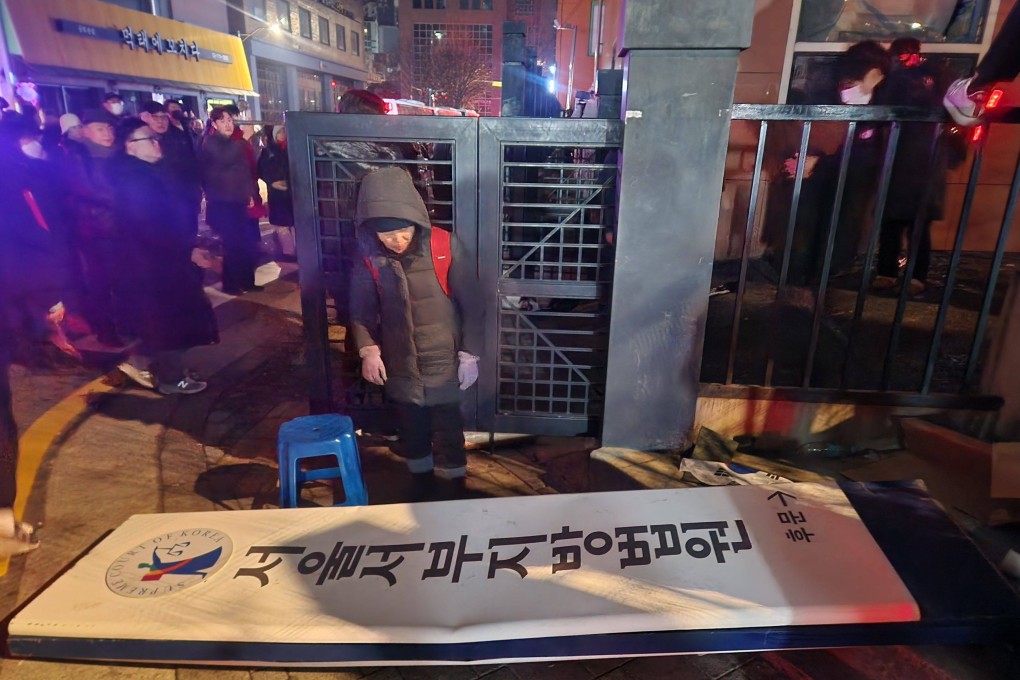 Supporters of impeached South Korean President Yoon Suk-yeol walk past a broken signboard at the Seoul Western District Court on Sunday. Photo: Yonhap via AFP