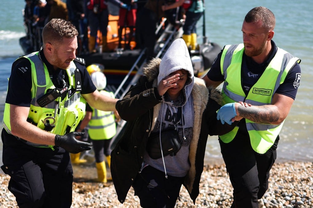 An interforce officer and a border force officer help a woman on the beach at Dungeness on the southeast coast of England, on August 16, 2023. Photo: AFP
