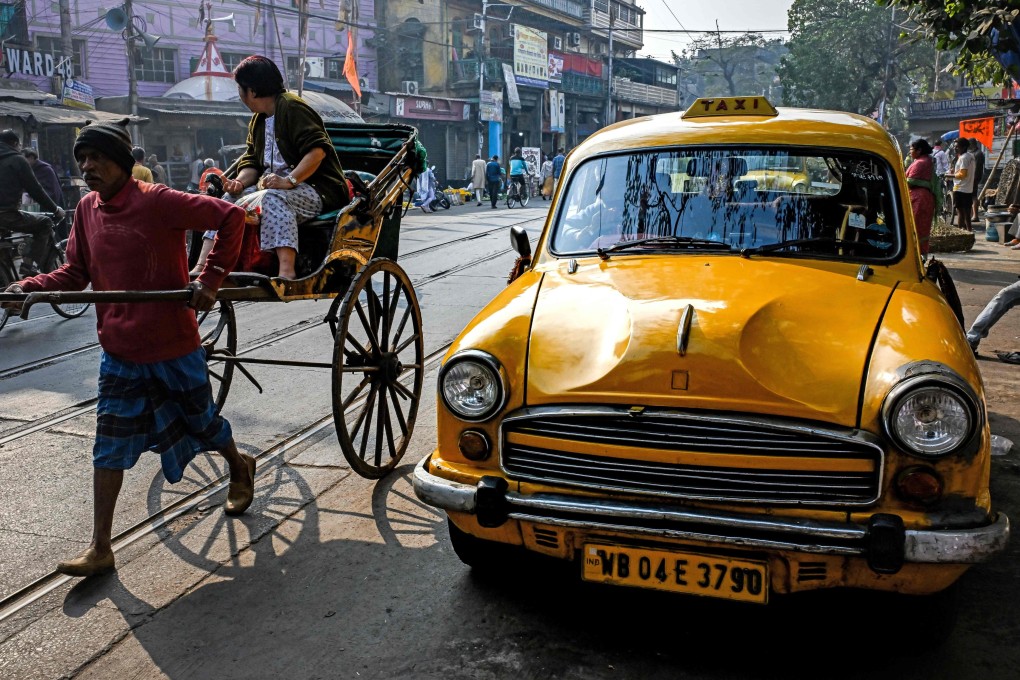 A woman rides a rickshaw past a Hindustan Ambassador yellow taxi, parked on a roadside in Kolkata. The one-time Indian capital is mourning the slow death of its stately yellow cabs. Photo: AFP