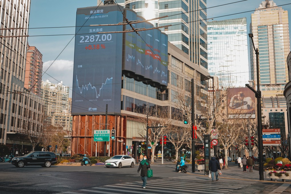 People cross a street near a screen showing stock exchange and economic data in Shanghai on February 5. Photo: EPA-EFE
