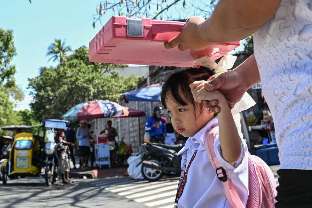 A man shields his daughter from the sun as they leave a school in Manila on Monday. Photo: AFP