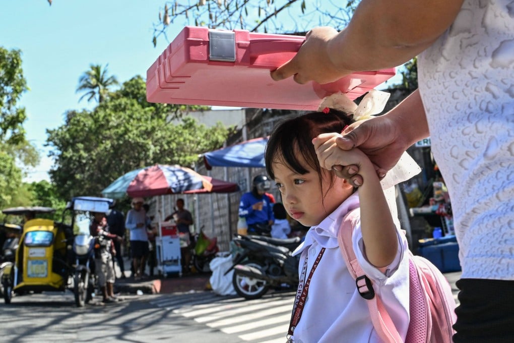 A man shields his daughter from the sun as they leave a school in Manila on Monday. Photo: AFP