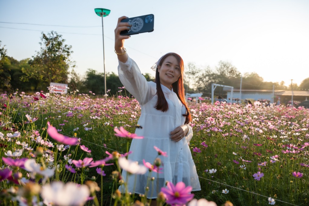 A woman takes a selfie amid blooming flowers at a park in Vientiane, Laos, on February 12, 2025. Vientiane offers a relaxed contrast to glitzy metropolises such as Bangkok and Singapore - if you are looking to party, you are in the wrong place. Photo: Xinhua