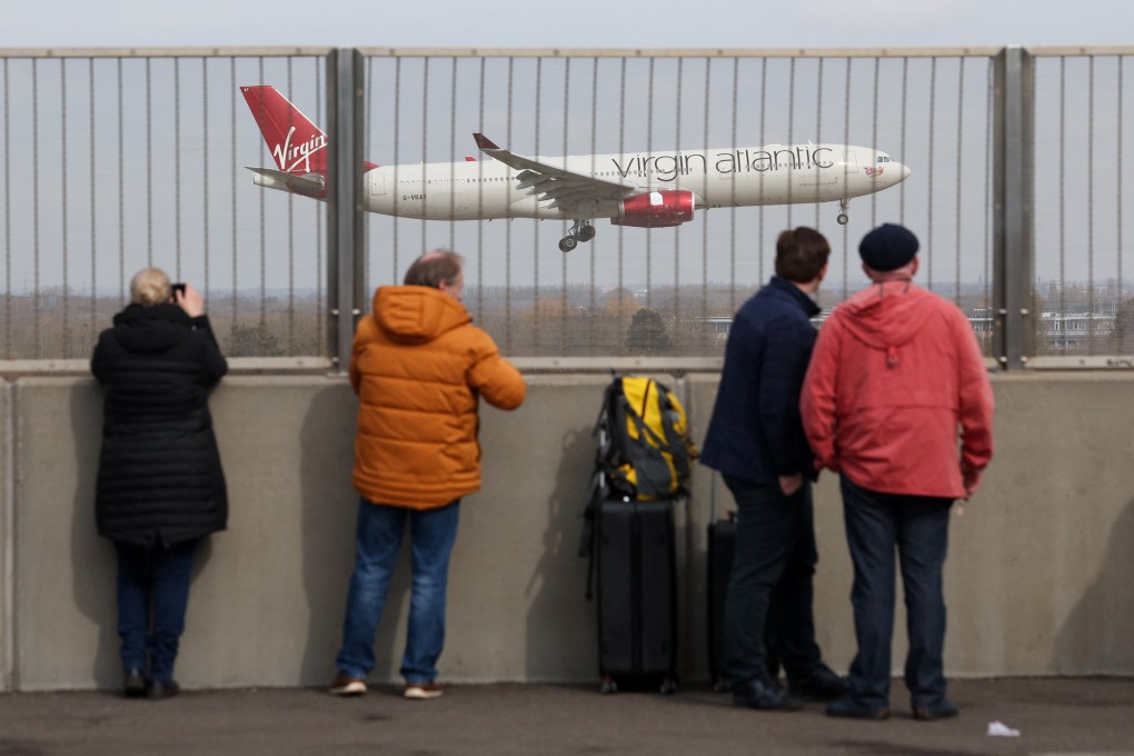 A plane flies past as people wait near the entrance at Terminal 5 of the Heathrow International Airport on Saturday. Photo: Reuters