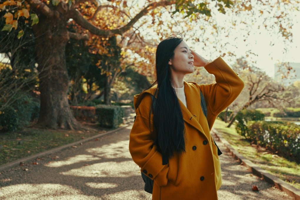 Woman, thinking and walk in Japanese park with smile in woods for travel on vacation, adventure and explore path. Gen z, student and happy on holiday in nature, forest and trail with trees in Kyoto