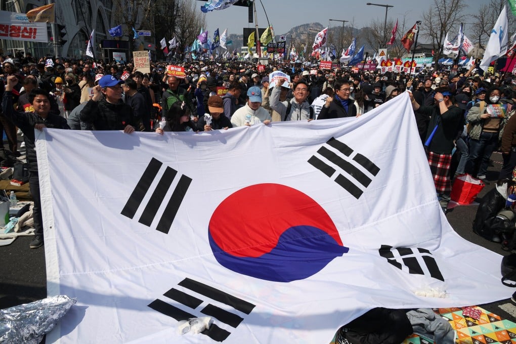 People hold up a South Korean flag as they celebrate Yoon Suk-yeol’s ouster in Seoul on Friday. Photo: Reuters