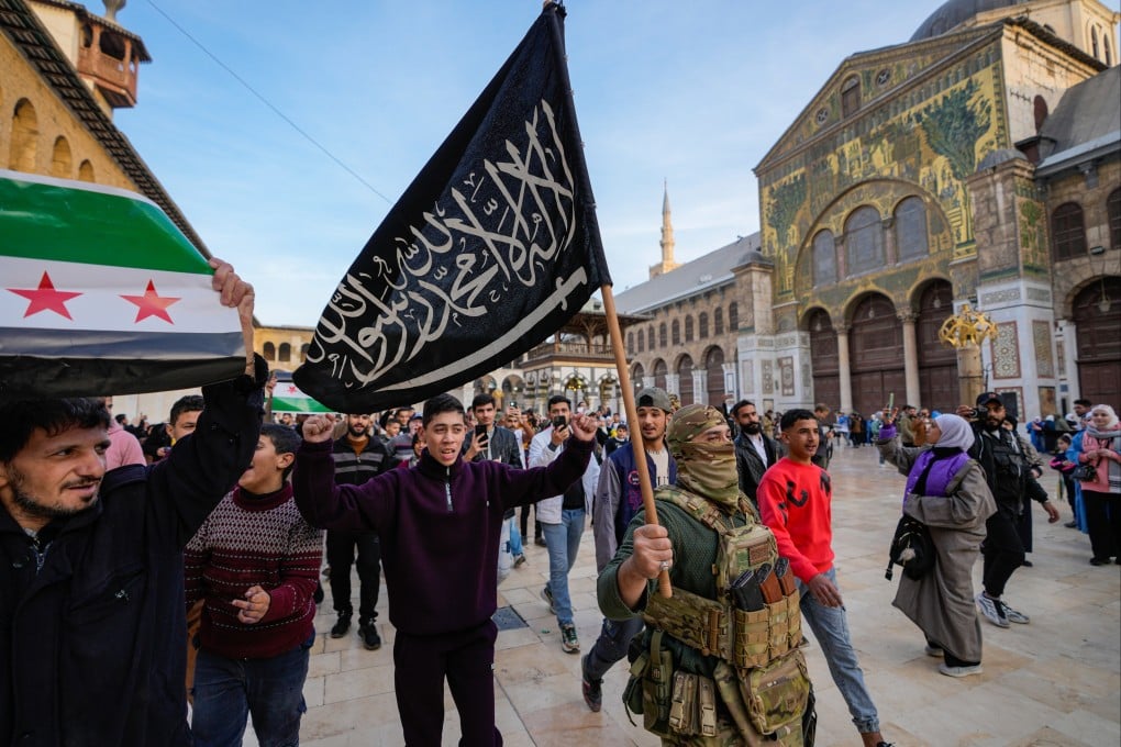 A masked opposition fighter carries a flag of Hayat Tahrir al-Sham (HTS) in Damascus, Syria on December 10. Members of HTS, deemed a terrorist group by the United Nations, now hold pivotal cabinet positions in Syria’s new government. Photo: AP