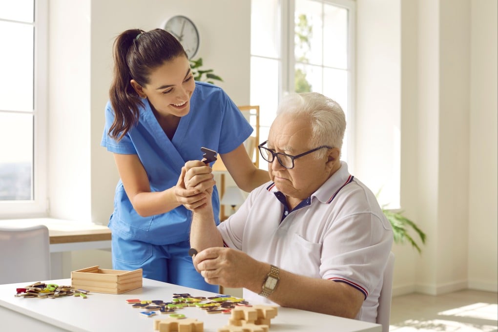Friendly caregiver or nurse in geriatric clinic or retirement home helping senior patient with puzzle. Photo: Shutterstock