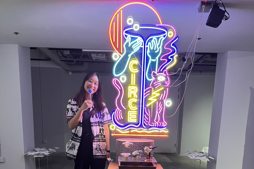 The artist Ho Sin-tung poses with a lollipop from her exhibition “Lucid Ruin” at Hong Kong art space Tomorrow Maybe next to the artwork at its entrance, called Circe Midway Island. Photo: Enid Tsui