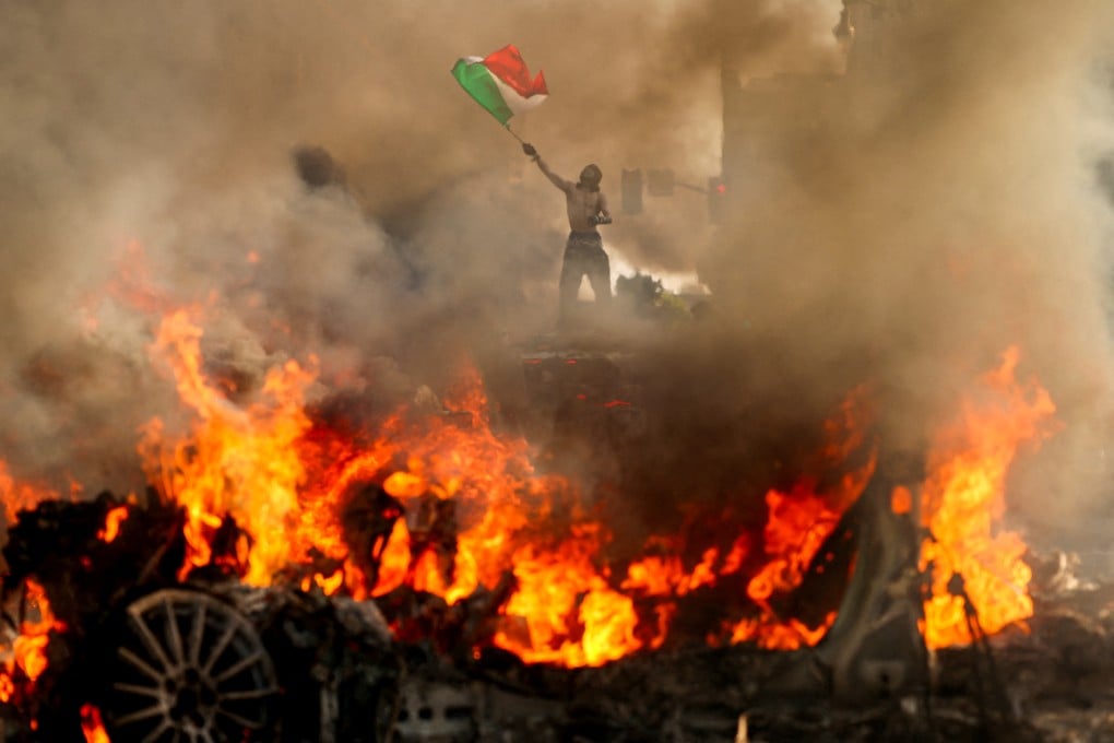 A demonstrator waves a Mexican flag as smoke and flames rise from a burning vehicle during protests against federal immigration sweeps, near Los Angeles City Hall in downtown Los Angeles on Sunday. Photo: Reuters