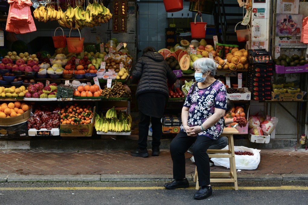 An elderly woman sits on a stool on the street in front of a fruit and vegetable seller in a market in Causeway Bay, Hong Kong, on December 26, 2024. Photo: Antony Dickson