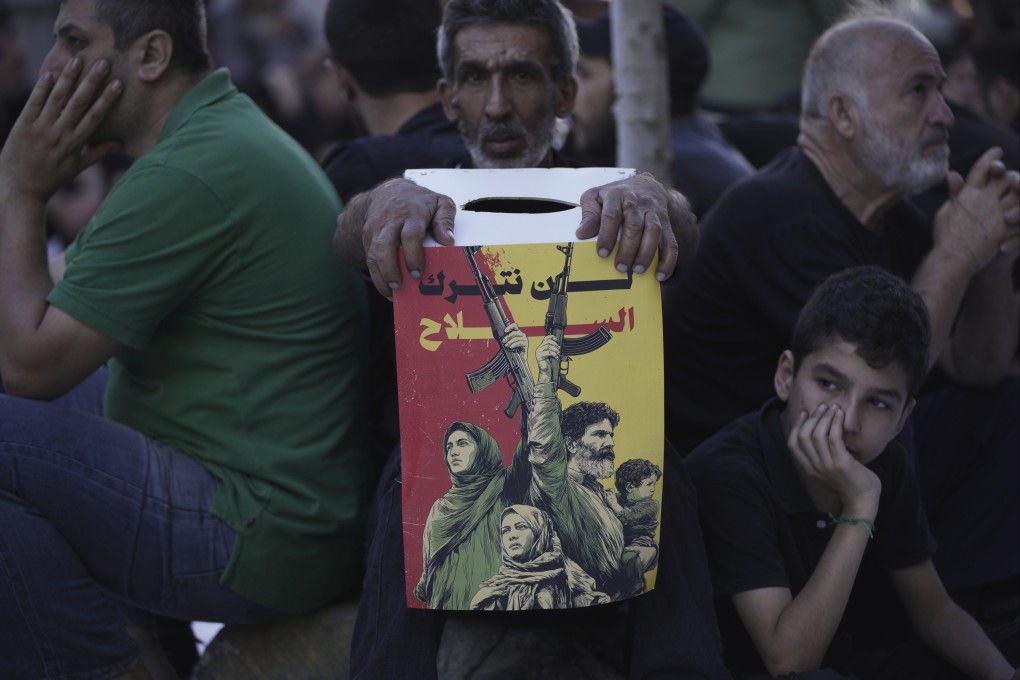 A Hezbollah supporter holds a poster reading ‘We shall not abandon our weapons’ as others listen during a Shiite sermon, in Beirut, Lebanon, on Sunday. Photo: AP