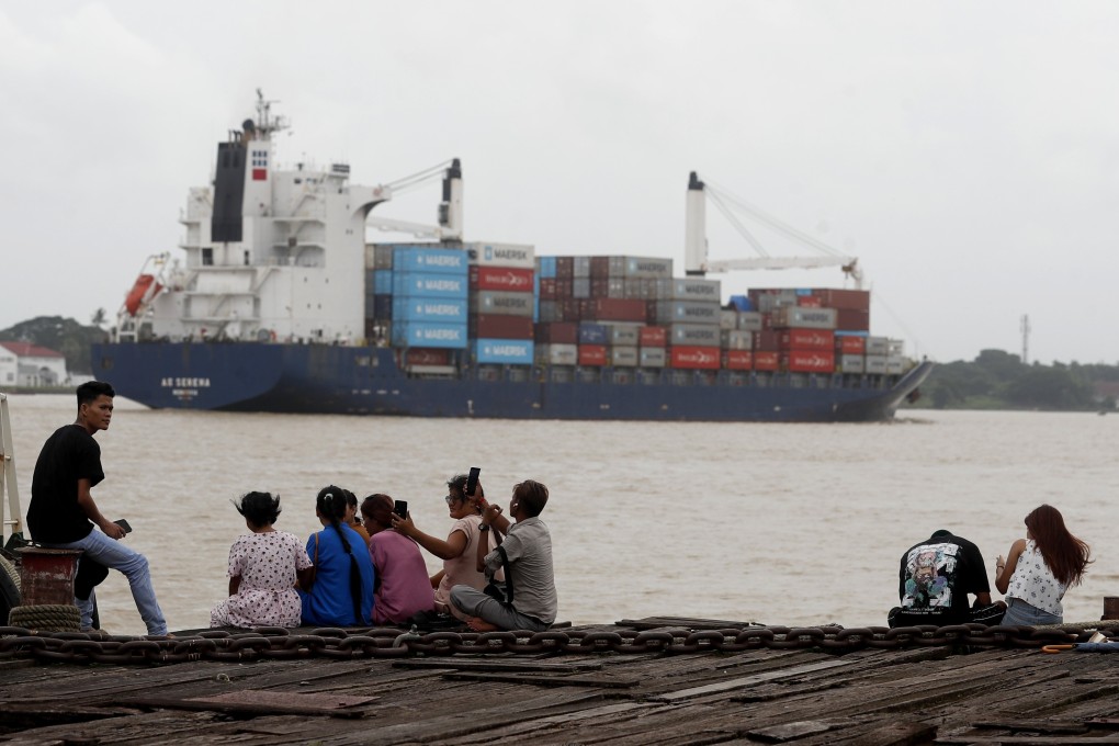 People relax at the jetty near the container cargo port on Wednesday as a container cargo ship passes by in Myanmar, which US President Donald Trump has threatened with a 40 per cent tariff. Photo: EPA