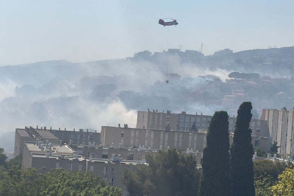A helicopter carries water to fight the wildfire on Tuesday. Photo: @thisisoim X via Reuters