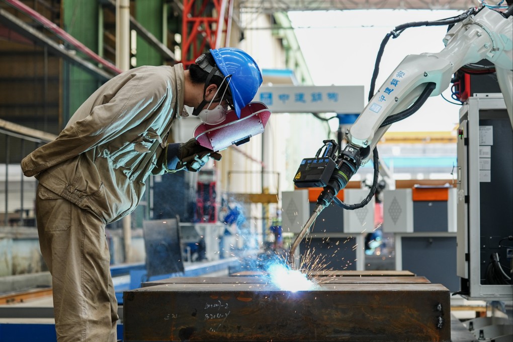 A worker cooperates with a robotic device to weld steel goods in Meishan, Sichuan province, on July 8. Photo: VCG / Getty Images