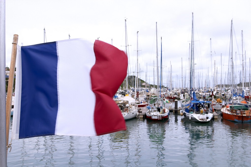 A French flag is seen in the foreground as and luxury yachts are moored at a port in Noumea, New Caledonia. Photo: Christina Pfeiffer