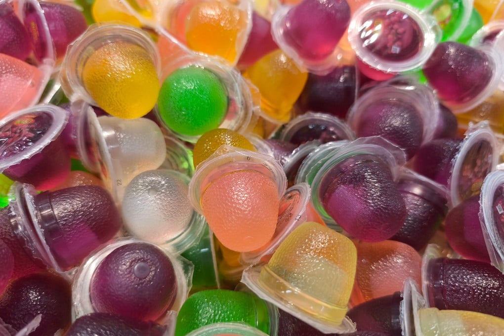 A pile of colorful konjac jelly candies in small plastic containers, with a warning label about choking hazards from the Centre for Food Safety, Hong Kong, 2025.