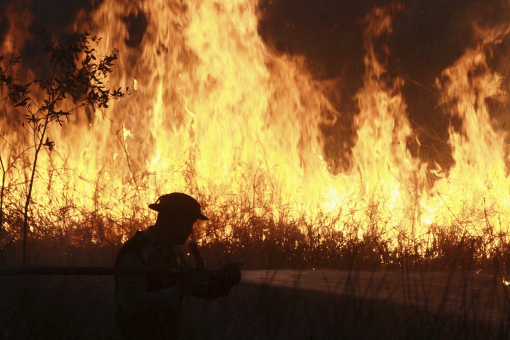 A police officer sprays water in a bid to extinguish a fire at a peatland field in Ogan Ilir, South Sumatra, Indonesia, on Sunday. Photo: AP