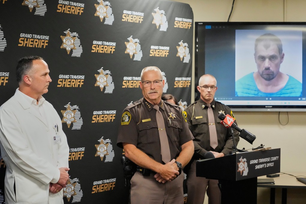 Grand Traverse County police at a news conference on Sunday in front of a booking photo of Bradford Gille, who is accused of stabbing 11 people at a Walmart in Traverse City, Michigan. Photo: AP