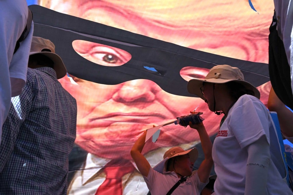 South Korean protesters tear a banner showing a caricature of US President Donald Trump as a robber during a rally in Seoul against Washington’s tariff policy on July 27. Photo: AFP