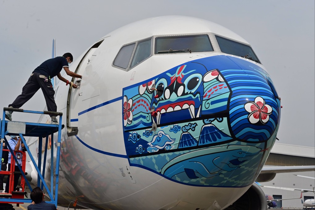 A worker closes a door of a Garuda Indonesia Boeing plane with a new face mask design. Garuda Indonesia, the country’s state-owned airline, is emerging from near-bankruptcy. Photo: AFP