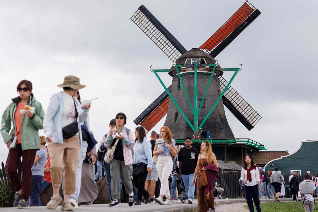 Tourists walk in front of a windmill in the Dutch village on Zaanse Schans on July 31, 2025. Featuring historic windmills and gabled wooden houses nestling by a meandering river, the picture-perfect and TikTok famous village has become “a national symbol of overtourism”, according to local authorities, who now want to charge a hotly contested entrance fee. Photo: AFP