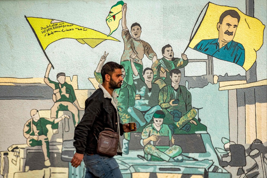 A man walks past a mural depicting supporters of the Syrian Democratic Forces (SDF), one of them raising a flag showing the face of Abdullah Ocalan -- founding member of the militant Kurdistan Workers’ Party (PKK) outlawed by Turkey, in Syria’s northeastern city of Qamishli on December 16 last year. Photo: AFP