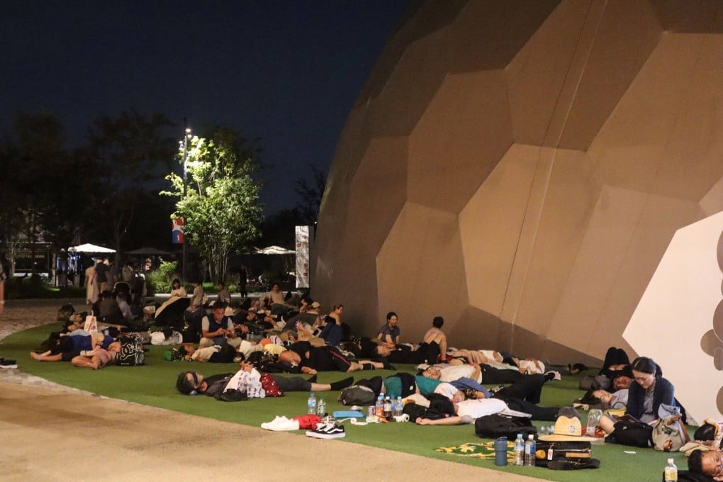 Visitors sleep outside one of the venues overnight after a power outage abruptly shut down the Osaka Metro line linking the city to the 2025 Osaka Expo site, early on Thursday. Photo: Jiji Press / AFP
