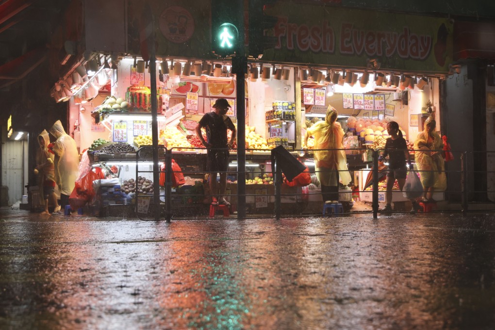People stand on stools outside a fruit store in Sai Ying Pun as the road floods during a black rainstorm warning on August 5. Photo: Karma Lo