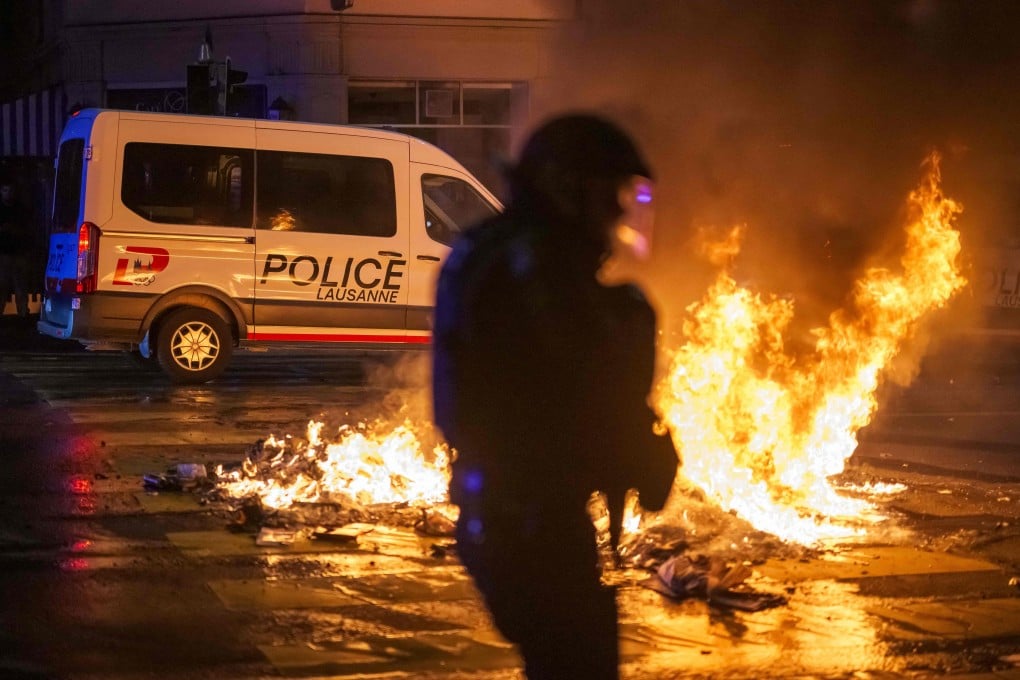 A police officer in riot gear walks past a fire in a street in Lausanne, on Monday, during a second night of rioting following the death of a teenager who tried to escape local police while driving a stolen scooter. Photo: AFP