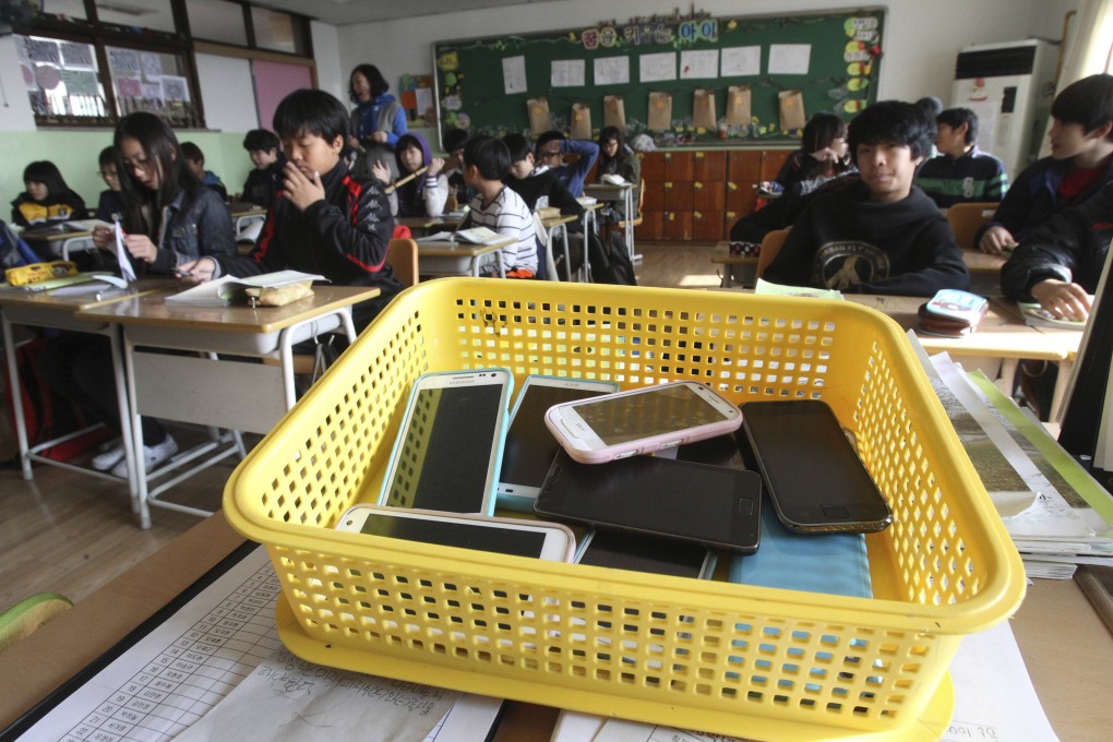 Smartphones are collected from students and placed in a plastic basket during a class in Suwon, South Korea. Starting in March, smartphones will be banned in classrooms across the country. Photo: