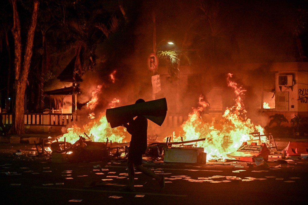 A protester carries looted goods on a street in front of a police headquarters that was set ablaze and looted during demonstrations in Surabaya on August 31. Photo: AFP