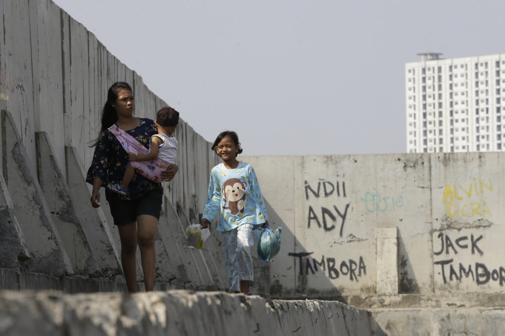 People walk near of a giant sea wall in Jakarta, which is used to prevent sea water from flowing into land and flooding it. Photo: AP