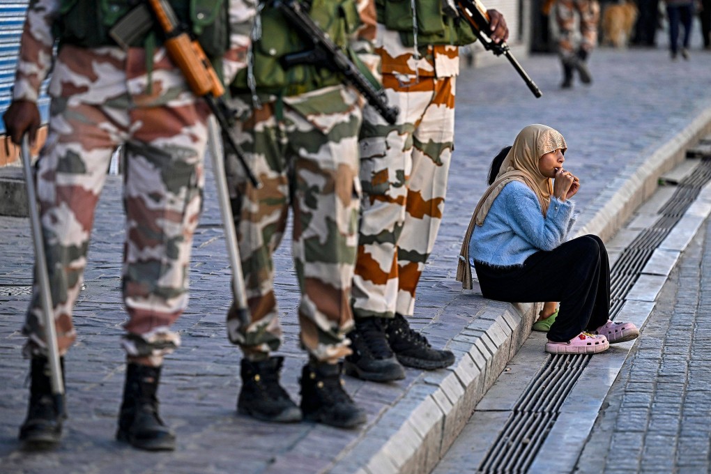 Security personnel stand guard near closed shops as a girl enjoys a chocolate sitting on a pavement after curfew was partially relaxed for a few hours in Leh on September 27. Photo: AFP