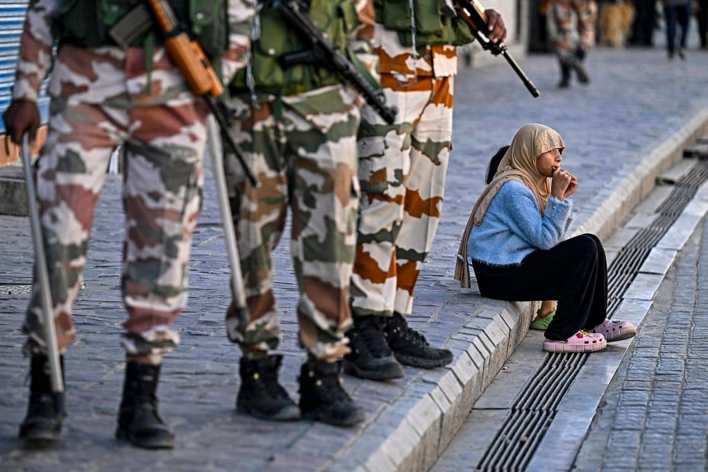 Security personnel stand guard near closed shops as a girl enjoys a chocolate sitting on a pavement after curfew was partially relaxed for a few hours in Leh on September 27. Photo: AFP