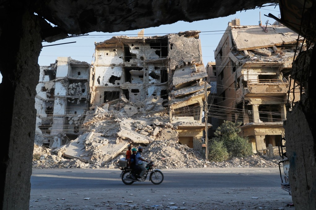 Residents on a motorcycle ride past war-damaged buildings in a suburb of Damascus, Syria. Photo: AP