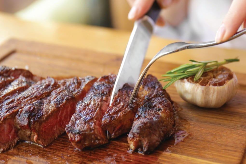 A woman cuts into a steak in a restaurant. A party in Malaysia is asking for beef to not be served during government functions. Photo: Shutterstock