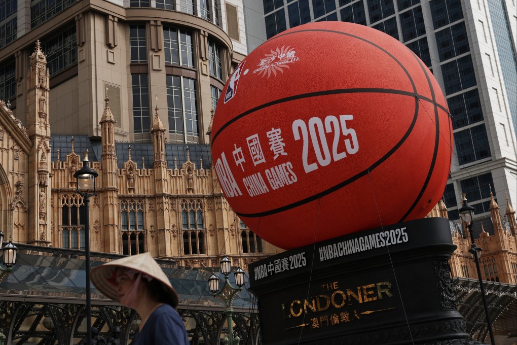 A woman wearing a straw hat walks pass a sign announcing the NBA China games in Macau. Photo: EPA