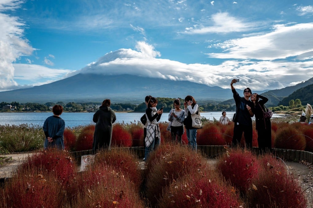 Tourists take pictures as cloud-clad Mount Fuji is seen in the background from Oishi park in the town of Fujikawaguchiko, Yamanashi prefecture, Japan, on Saturday. Photo: AFP