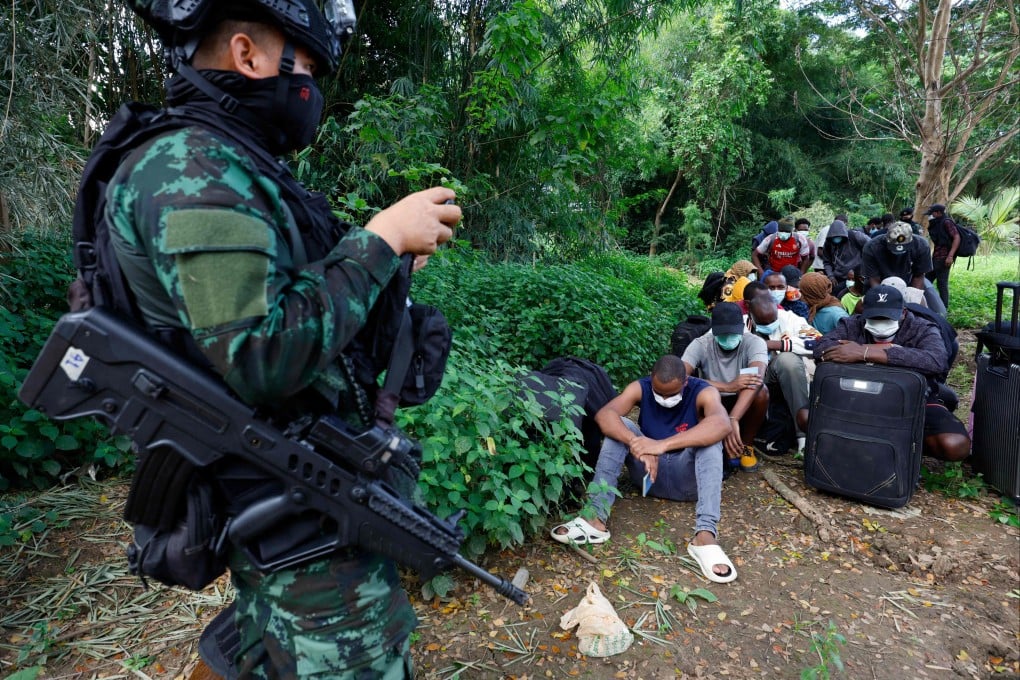 A soldier stands guard as people from various countries, who were working in the KK Park compound in Myanmar and crossed to Thailand via the Moei river, sit in Mae Sot District, Tak province on Friday. Photo: AFP
